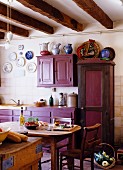 Französische Landhausküche mit auberginefarbenen Schränken und rustikalem Essplatz in einem Bauernhaus