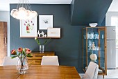 Glass vase of flowers on wooden table below pendant lamp with spherical glass lampshades and display case against black-painted wall