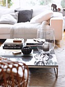 Candle in large glass vase and stacked books on low coffee table in front of white couch with scatter cushions
