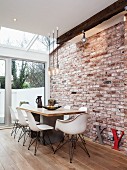 White shell chairs at dining table on wooden floor surrounded by exposed brickwork and modern conservatory glazing