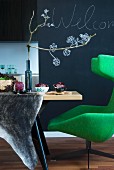 Grüner Designer Ohrensessel mit Esstisch und herbstlicher Tischdekoration mit aufgemalten Blüten an der Tafellack Wand im Hintergrund