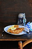 Wiener Schnitzel (breaded veal escalope from Vienna) with lemon wedges on a rustic table with a tankard of beer in the background