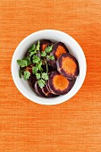 Slices of purple carrots in a white bowl with coriander leaves