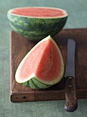 A mini watermelon with a knife on a wooden board