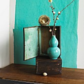 Bird's nest on wooden cabinet behind turquoise vase of flowering twigs