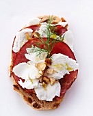 A slice of bread topped with cream cheese, ham and hazelnuts
