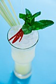A cocktail garnished with lemongrass, mint and a chilli pepper