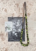 Grüne Kette aus Samenkapsen von der Nigellablume und Schwarzweissbild mit Blumenstrauss Motiv, an Wand mit verblichenem Ornamentmuster