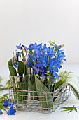 Larkspur and cutlery in glasses wrapped in hosta leaves