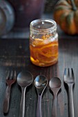 A jar of pumpkin and orange marmalade with spoons and forks in front of it