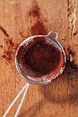 Cocoa powder in a sieve on wooden surface
