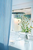 Candle lantern and tealight holders on white windowsill with pale blue striped curtain
