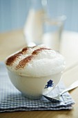 Cup of cappuccino with foamed milk on blue and white, country-house-style gingham serviette