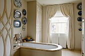 Collection of decorative plates above wood-clad bathtub with marble edge in stylish, English bathroom