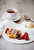 A waffle with vanilla ice cream, chocolate sauce and strawberries