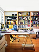 Woman sitting at large, corner desk in study with bookcase in background