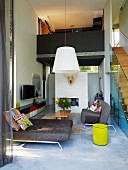 Designer sofas in open-plan, double-height living area with staircase leading to gallery bridge