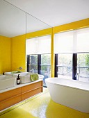Renoviertes Badezimmer mit sonnengelben Mosaikfliesen und Spiegelwand hinter Waschkommode mit Aufsatzbecken
