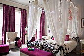 Four-poster bed decorated with fairy lights and purple textiles in elegant bedroom