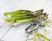 Green asparagus with a peeler on a wooden surface