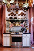 Pots, pans and old bundt cake tins hanging over kitchen counter with stainless steel cooker