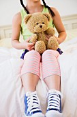 Girl sitting on bed holding teddy bear