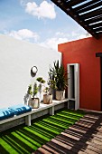 Pattern of light and shade on sheltered terrace with green floor and white, protruding window frame in brick red wall