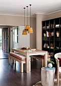 Pendant lamps above pale wood dining set with cushions on benches; ornaments on dark shelves in background