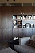 Books and pictures on shelves of dark living room cupboards; grey sofa in foreground