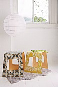 Laminated wood stools covered in patterned wallpaper below round, white paper lampshade