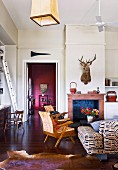 Living room with rustic ambiance; 50s-style armchairs in front of open fireplace below hunting trophy