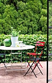 View through open terrace door of colourful folding chairs and garden table in front of ivy-covered wall and woodland backdrop