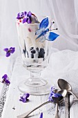 An ice cream sundae with vanilla ice cream, fruit jelly and blueberries, and decorated with sugared violets