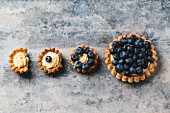 Various different sized blueberry tartlets with lemon cream, one with a bite taken out