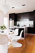 White designer shell chairs and table on wooden floor in front of modern counter and black fitted kitchen cupboards
