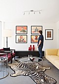 Lounge area with round coffee table on zebra-skin rug, man standing next to low black sideboard below framed pictures with Chinese motifs on wall