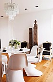 weiße Designer-Schalenstühle um Tulip Table, im Hintergrund antike Sessel mit schwarzen Polstern und antike, asiatische Holzstelen an Wand in minimalistischem Wohnraum