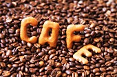 The word 'cafe' written using alphabet biscuits on top of coffee beans