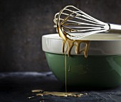 Cake mixture dripping off a whisk balanced over a ceramic bowl