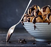A bowl of profiteroles with chocolate sauce and a spoon