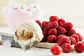 Vanilla and raspberry ice cream in an ice cream scoop next to a pile of fresh raspberries