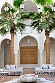 Moroccan courtyard with spherical lamps above fountain and seating around palm trees in front of arcade