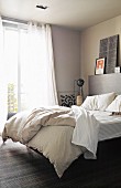 View through open door of double bed below window with airy curtains in bedroom