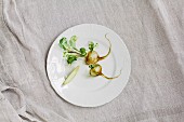 White turnips with leaves and a slice of turnip on a white porcelain plate