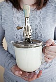 A woman holding a measuring jug of cream and an old hand mixer
