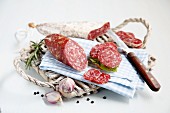 Salami on a board with a blue and white checked napkin, a knife and onions