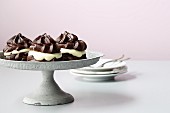 Chocolate profiteroles on a grey cake stand in front of a stack of plates with forks