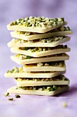 A stack of white chocolate with pistachios on a purple surface