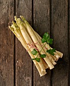 A bunch of fresh white asparagus with a sprig of parsley on a wooden surface