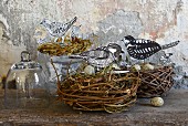 Selbstgebastelte Papier Vögel und Wachteleier in Vogelnestern auf Holzablage, vor Wand mit abblätternder Farbe